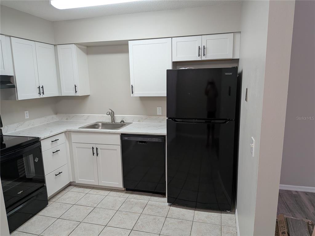 A kitchen features white cabinets, black appliances, and light-colored countertops with a tiled floor — 1020 HOWELL UNIT A7, BROOKSVILLE, FL