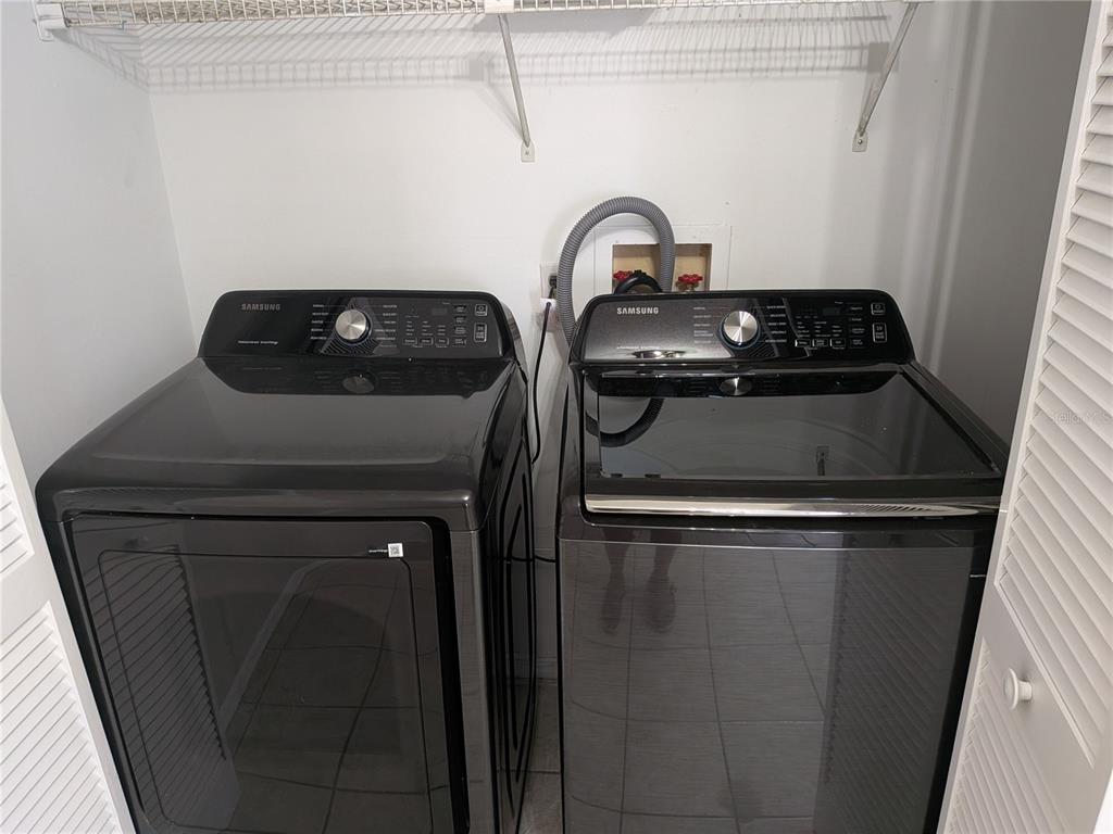 A laundry closet contains a black Samsung washer and dryer set beneath a wire shelf — 1020 HOWELL UNIT A7, BROOKSVILLE, FL
