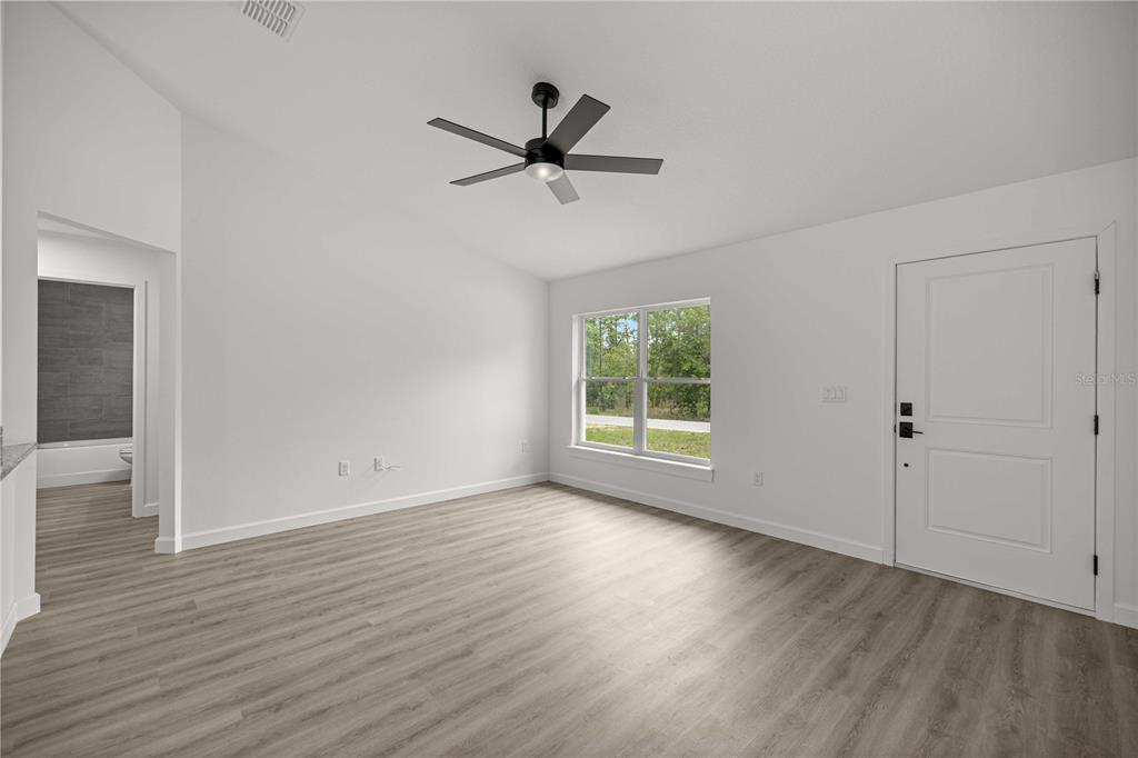 An empty room with light wood-look flooring, white walls, a ceiling fan, and an exterior door — 24128 NW GERANIUM AVENUE, DUNNELLON, FL