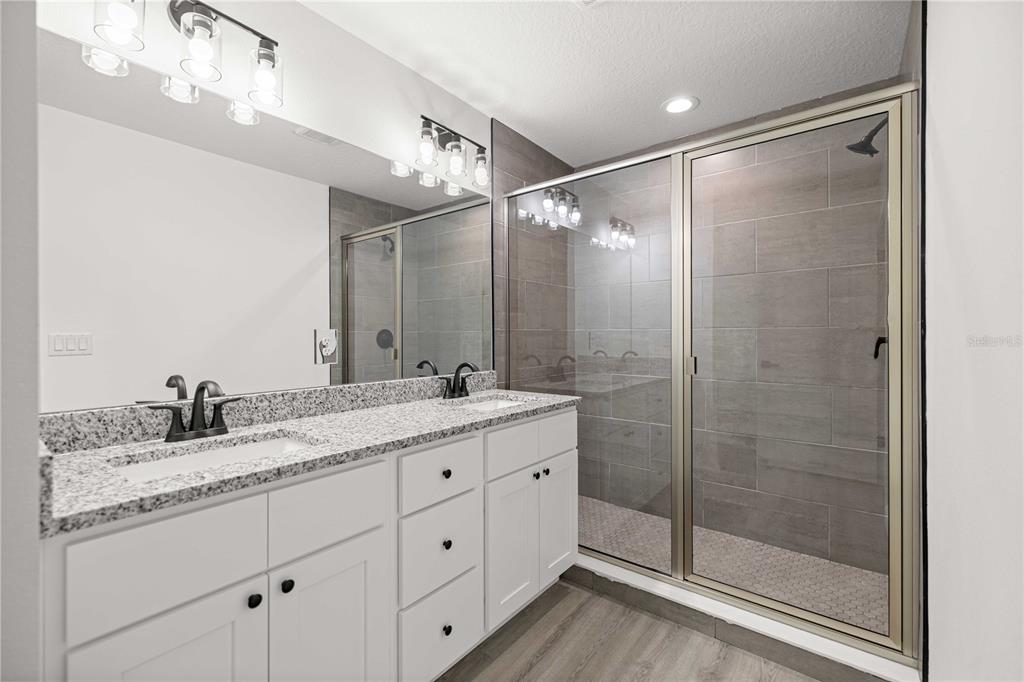 A bathroom features a double vanity with granite countertops, white cabinets, and a tiled shower — 24128 NW GERANIUM AVENUE, DUNNELLON, FL