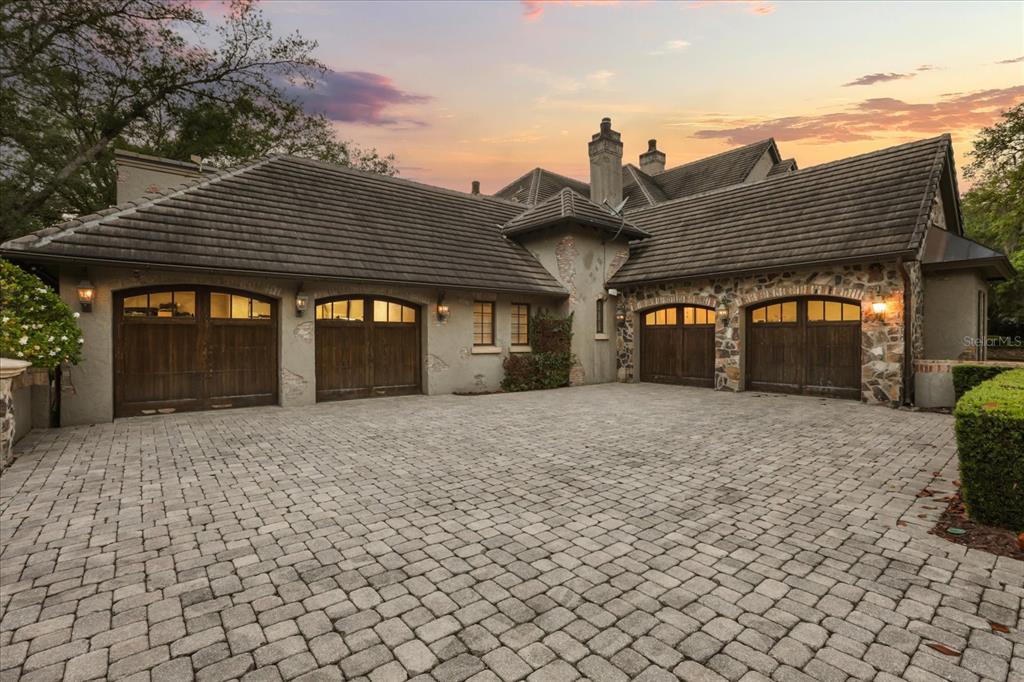 A four-car garage with arched wooden doors and stone accents faces a paved driveway — 2878 MARKHAM WOODS ROAD, LONGWOOD, FL