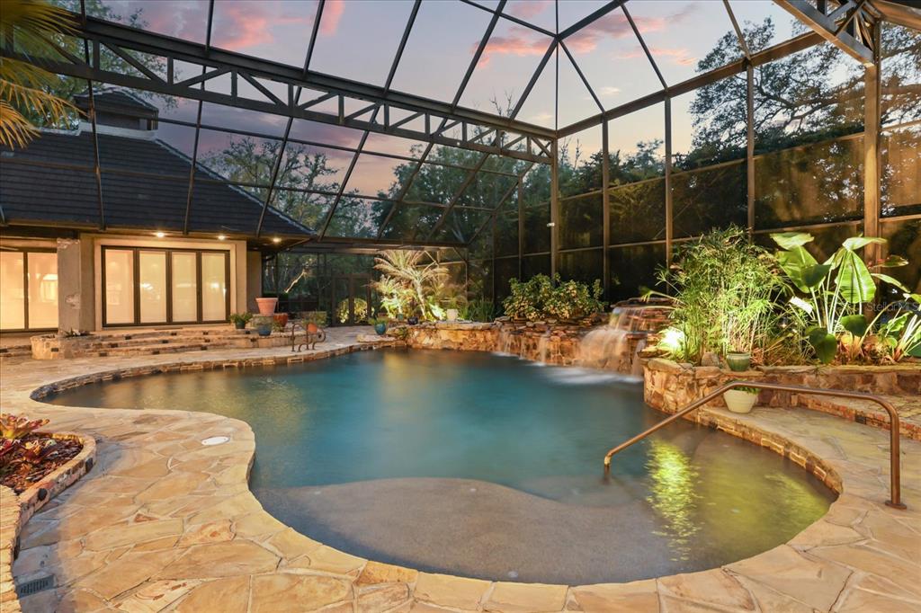A screened-in pool area features a stone deck, a rock waterfall, and tropical landscaping — 2878 MARKHAM WOODS ROAD, LONGWOOD, FL