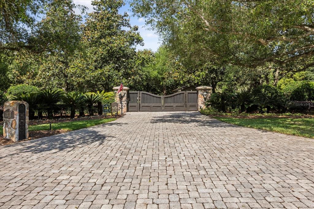 A paved driveway leads to a gated entrance surrounded by lush trees and landscaping — 2878 MARKHAM WOODS ROAD, LONGWOOD, FL
