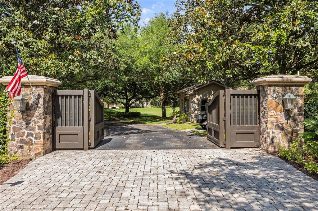 A stone-pillared gated entrance leads to a paved driveway shaded by large, mature trees — 2878 MARKHAM WOODS ROAD, LONGWOOD, FL