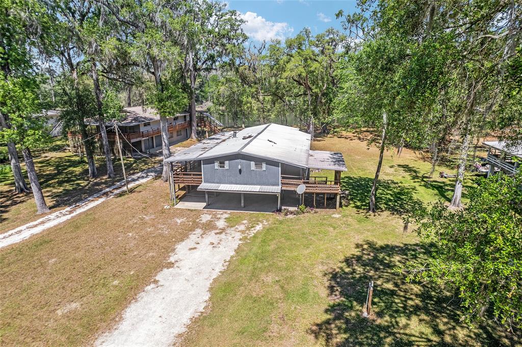 An elevated gray house with a metal roof sits on a grassy, tree-filled lot — 7870 SW 25TH PLACE, BELL, FL