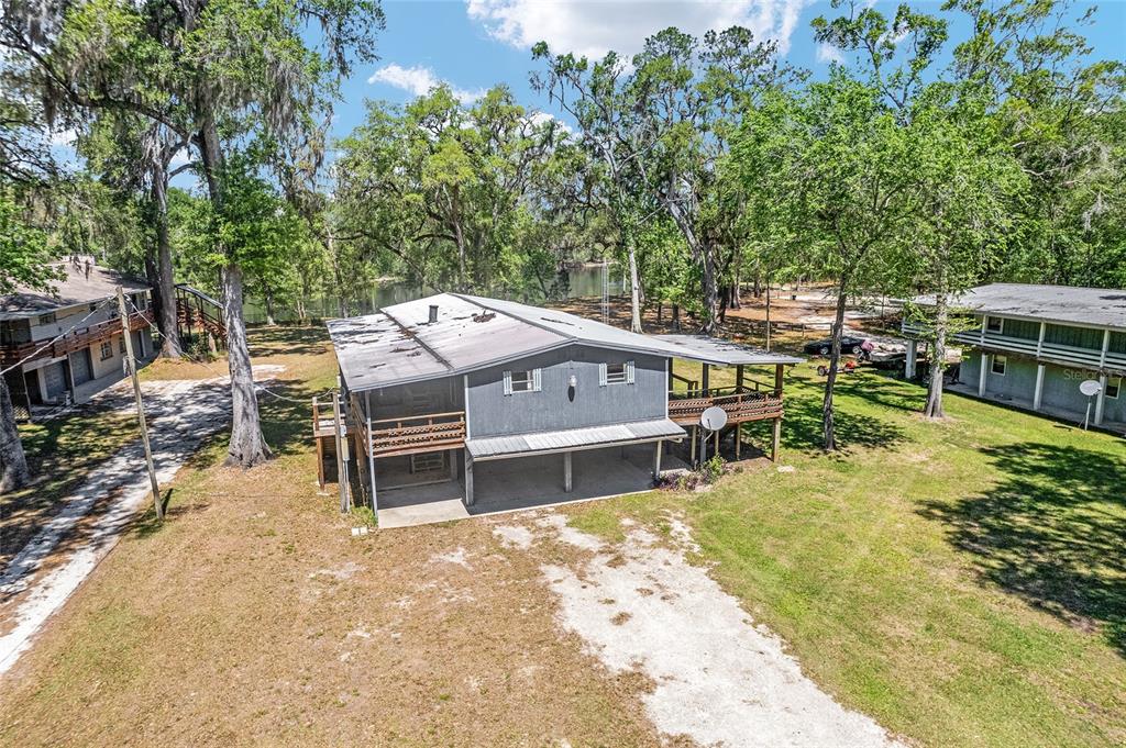 An elevated gray house with a metal roof sits on a grassy lot near trees — 7870 SW 25TH PLACE, BELL, FL