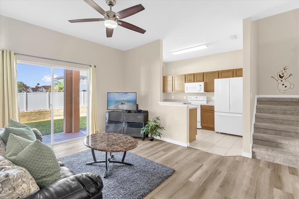 A living room with wood-look flooring, a ceiling fan, and an adjacent open kitchen — 1144 CALABRIA AVENUE, DAVENPORT, FL