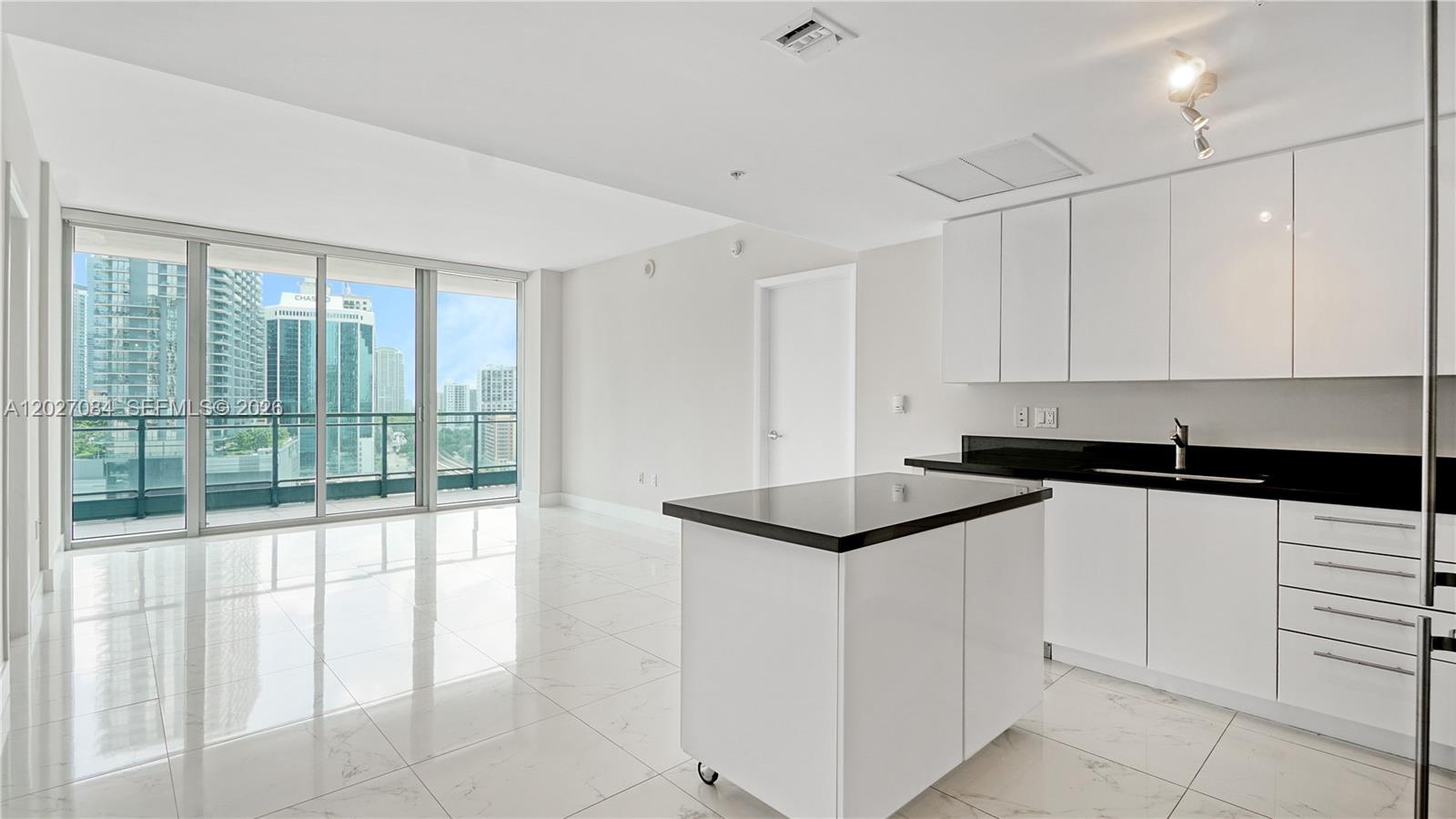 A modern kitchen with white cabinets and a black island overlooks a city skyline — 92 SW 3rd St # 1803, Miami FL 33130, MIAMI, FL