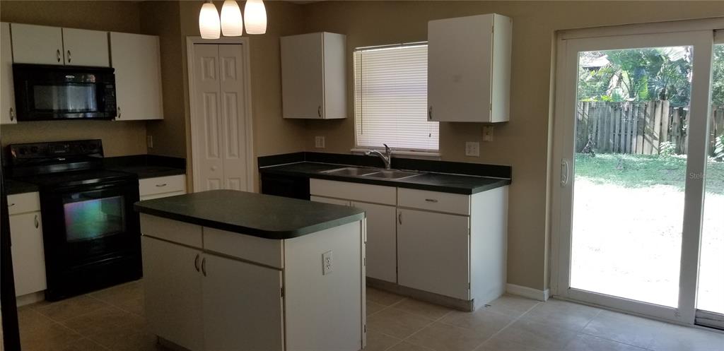 A kitchen features white cabinets, black appliances, a central island, and a sliding glass door — 4040 IVEYGLEN AVENUE, ORLANDO, FL