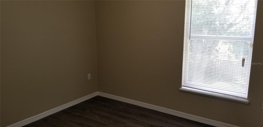 An empty room features beige walls, dark wood-look flooring, and a window with white blinds — 4040 IVEYGLEN AVENUE, ORLANDO, FL