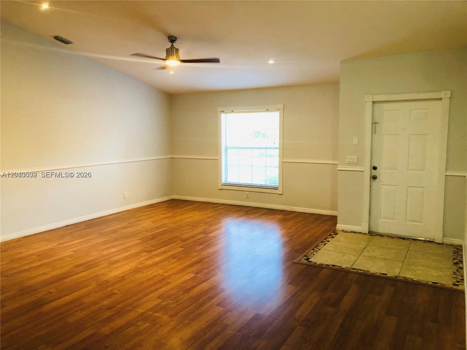 An empty living room features wood-look flooring, a ceiling fan, and a front entry door — 13677 Temple Blvd, West Palm Beach FL 33412, WEST PALM BEACH, FL