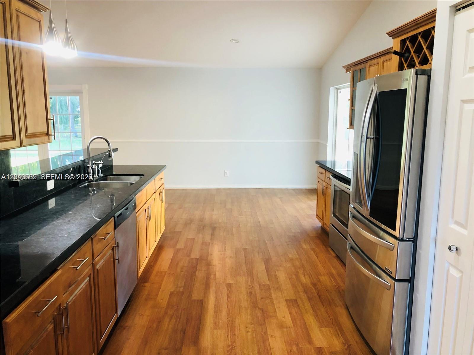 A kitchen features wood cabinets, black countertops, stainless steel appliances, and wood-look flooring — 13677 Temple Blvd, West Palm Beach FL 33412, WEST PALM BEACH, FL