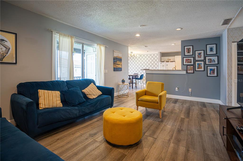 A living room features a blue sofa, yellow armchair, matching ottoman, and wood-look flooring — 3816 CORTEZ DRIVE UNIT D, TAMPA, FL