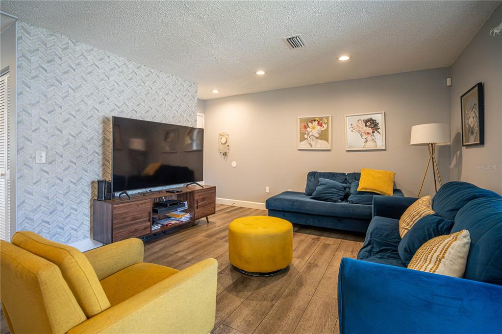 A living room features blue sofas, a yellow armchair, a yellow ottoman, and a television — 3816 CORTEZ DRIVE UNIT D, TAMPA, FL