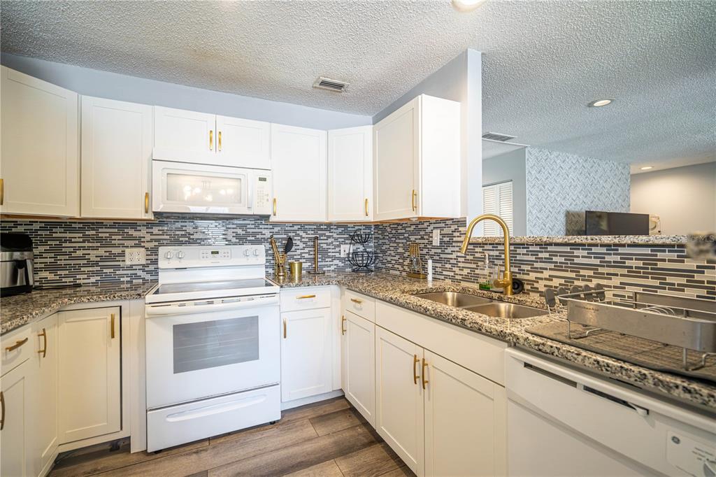 A kitchen features white cabinets, granite countertops, a tiled backsplash, and stainless steel appliances — 3816 CORTEZ DRIVE UNIT D, TAMPA, FL
