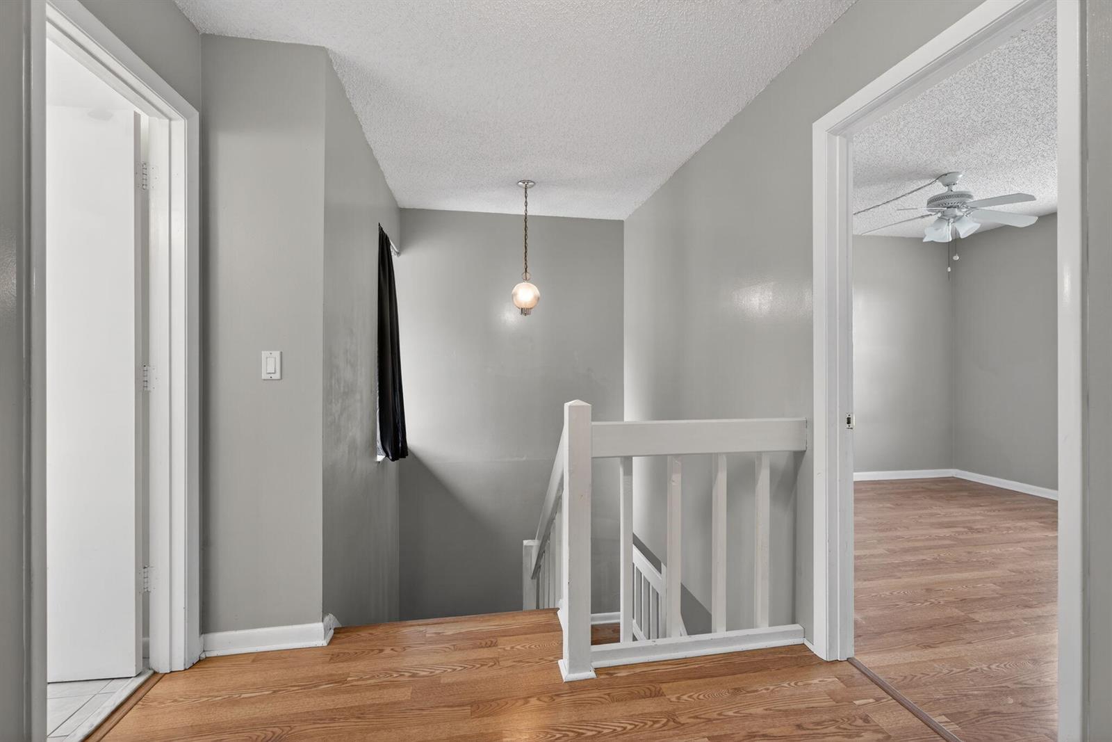 A hallway with wood flooring, a staircase with white railings, and a hanging pendant light — 707 Stonewood Court # 19c, Jupiter FL 33458, JUPITER, FL