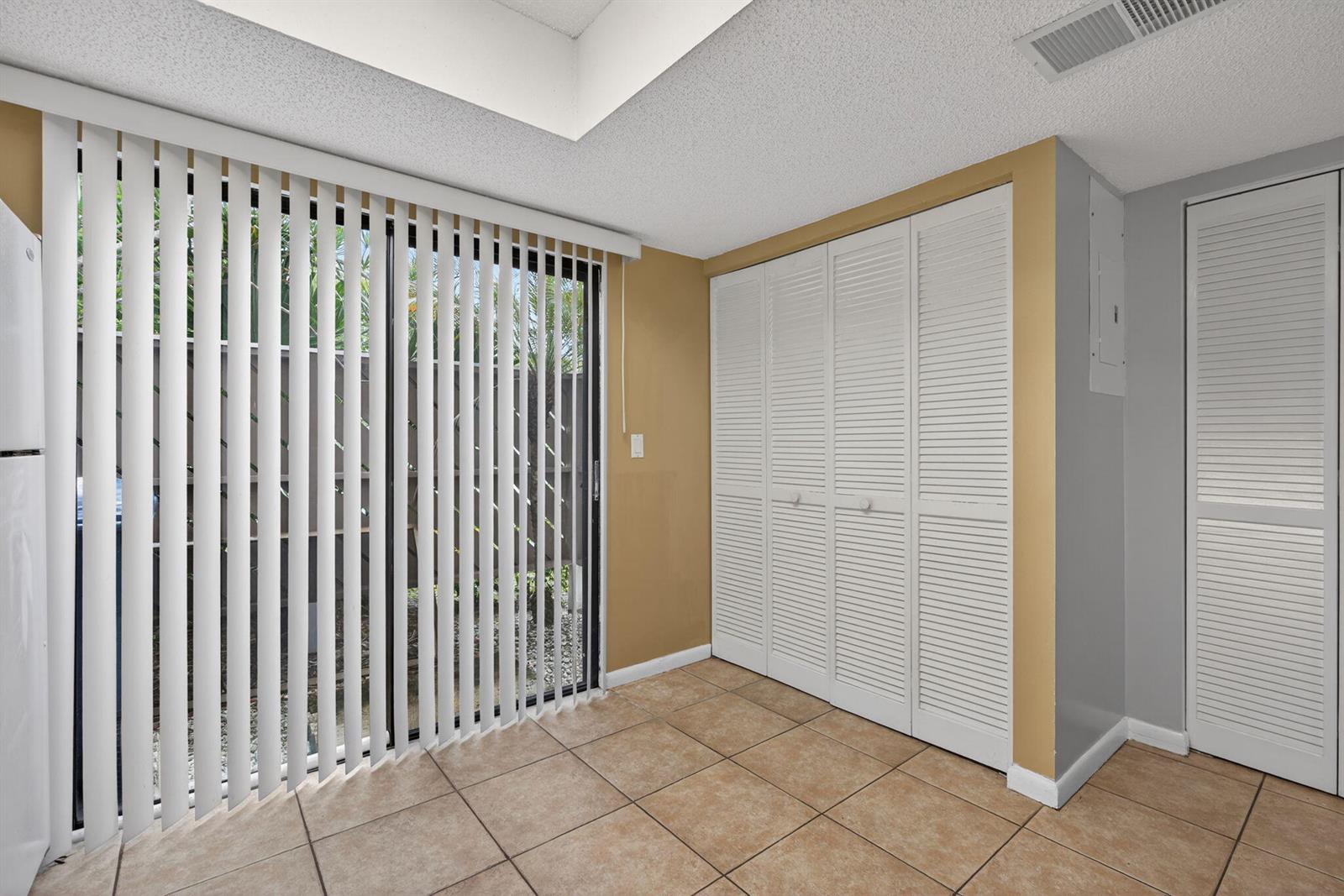 A room with tiled floors, a sliding glass door with vertical blinds, and louvered closet doors — 707 Stonewood Court # 19c, Jupiter FL 33458, JUPITER, FL