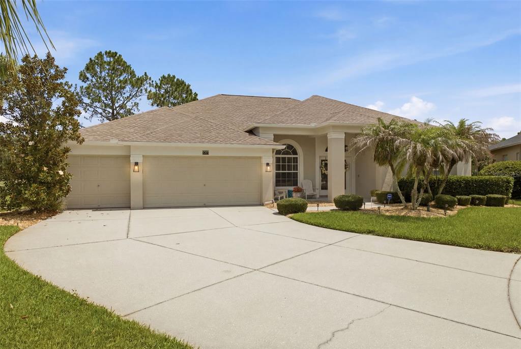 A single-story house with a beige exterior, a three-car garage, and a concrete driveway — 25651 FERDINAND COURT, WESLEY CHAPEL, FL