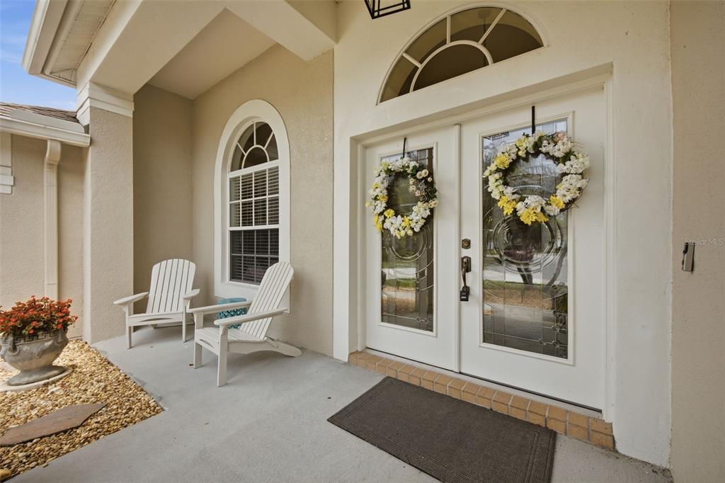 A covered front porch features two white Adirondack chairs, a potted plant, and double doors — 25651 FERDINAND COURT, WESLEY CHAPEL, FL