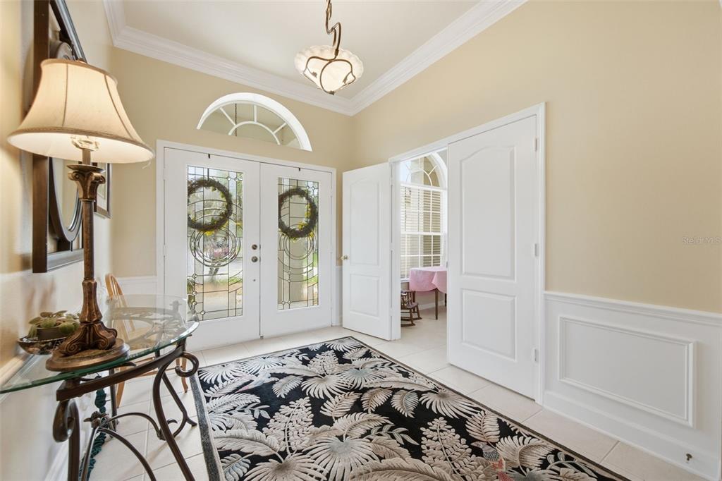 An entryway features a patterned rug, a glass-topped table, a lamp, and double front doors — 25651 FERDINAND COURT, WESLEY CHAPEL, FL