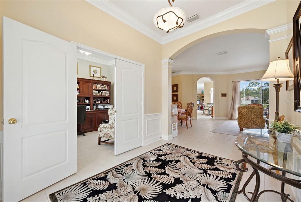 A foyer with a patterned rug leads into a home office and an open living area — 25651 FERDINAND COURT, WESLEY CHAPEL, FL