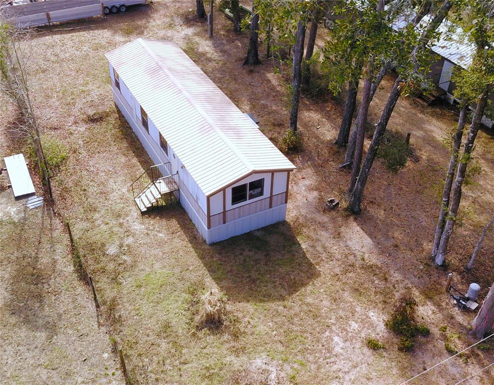 An aerial view shows a single-wide mobile home situated on a wooded, grassy lot — 7809 SW 12TH PLACE, BELL, FL