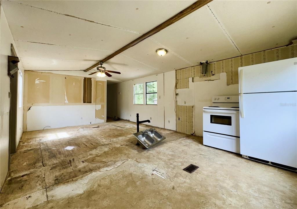 An unfinished kitchen and living area features exposed subflooring, a white stove, and a refrigerator — 7809 SW 12TH PLACE, BELL, FL