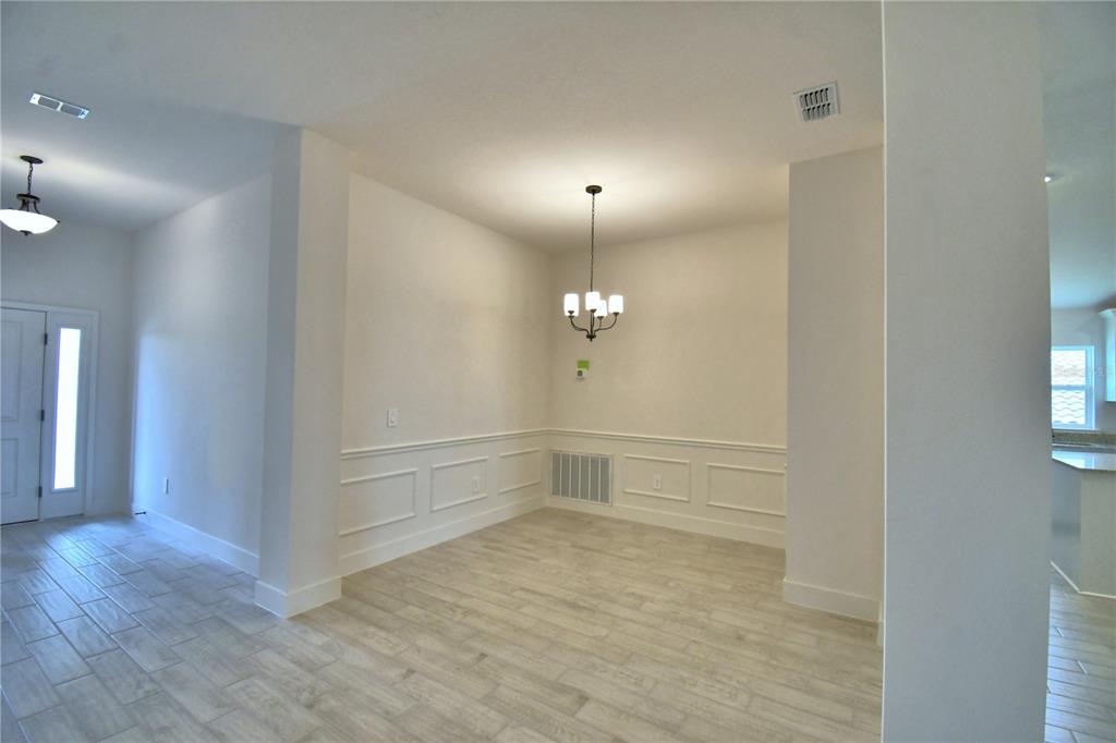 An open-concept interior features a tiled floor, white walls, support columns, and a kitchen area — 4616 CALAMINT LANE, AUBURNDALE, FL