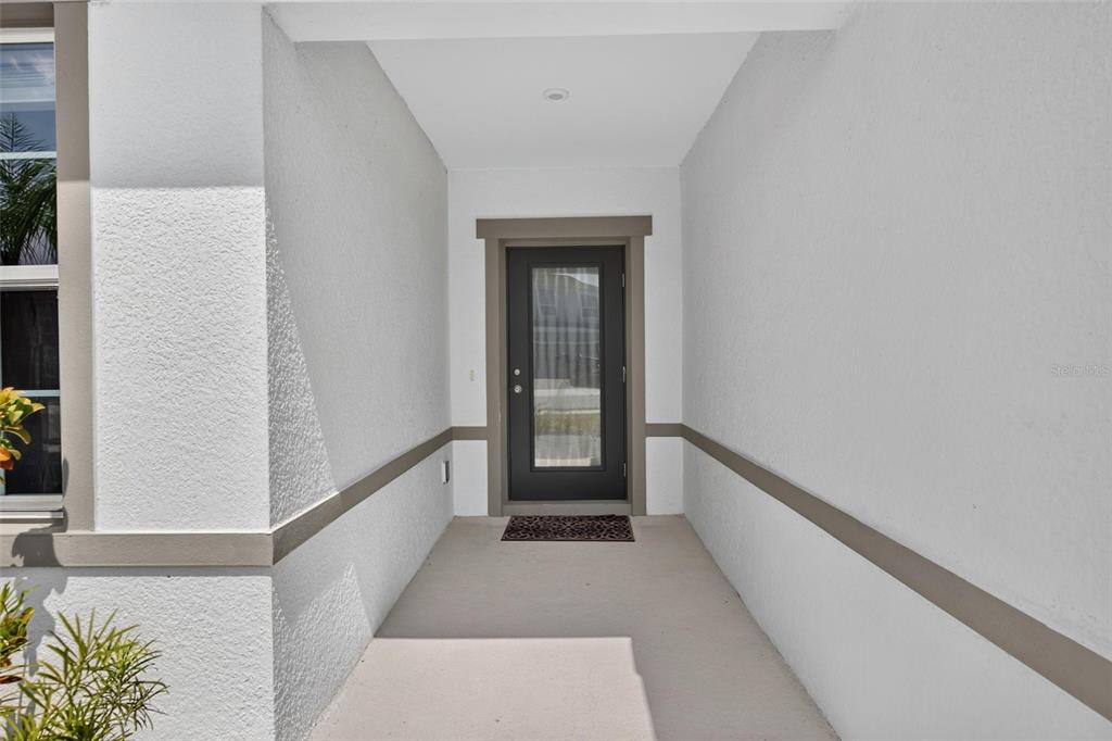 A covered entryway features a dark-framed glass door, white stucco walls, and a concrete floor — 153 EAGLE HARBOR WAY, DAYTONA BEACH, FL