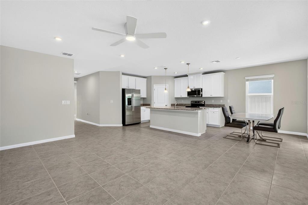 An open-concept kitchen and dining area features white cabinets, stainless steel appliances, and tile flooring — 153 EAGLE HARBOR WAY, DAYTONA BEACH, FL