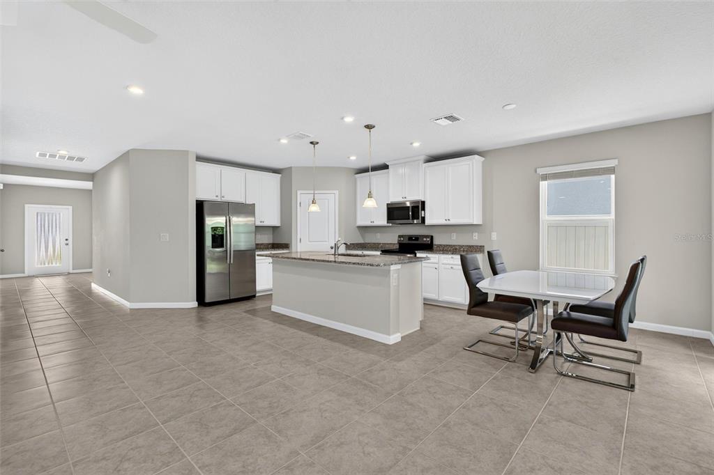 A kitchen features white cabinets, stainless steel appliances, a granite island, and tile flooring — 153 EAGLE HARBOR WAY, DAYTONA BEACH, FL