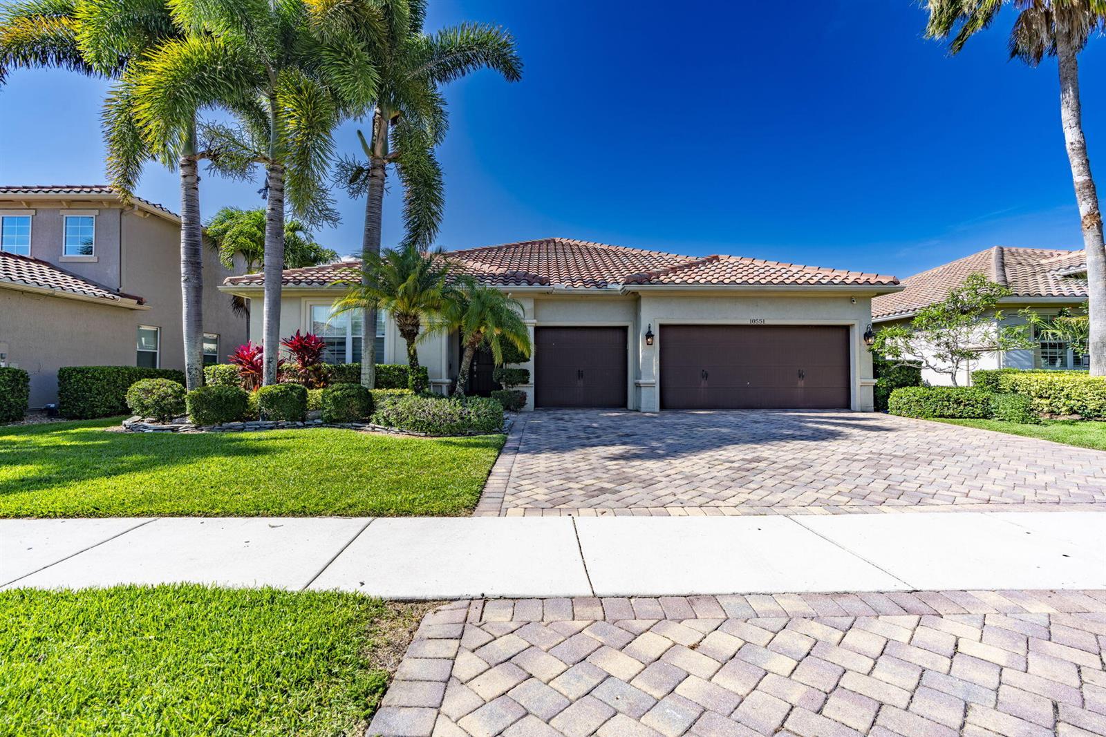 A single-story house with a tile roof, two garage doors, and palm trees in front — 10551 Long Leaf Lane, Wellington FL 33414, WELLINGTON, FL