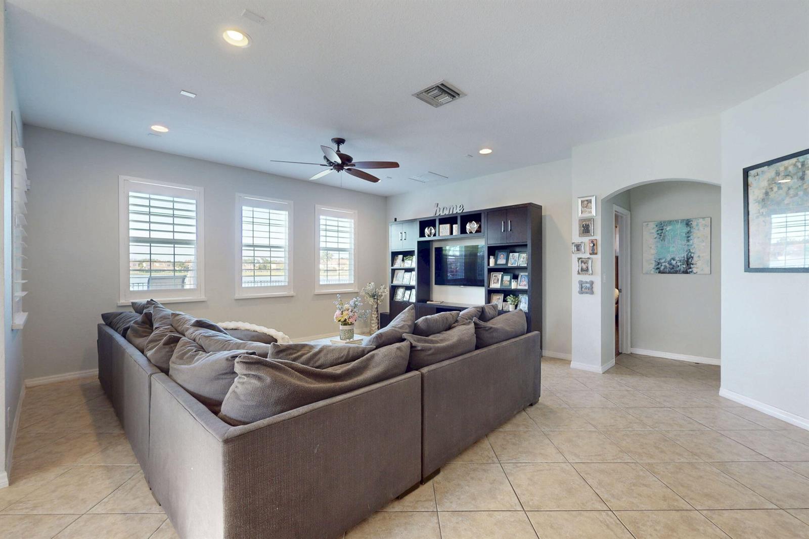 A living room features a large gray sectional sofa, a dark entertainment center, and tile flooring — 10551 Long Leaf Lane, Wellington FL 33414, WELLINGTON, FL