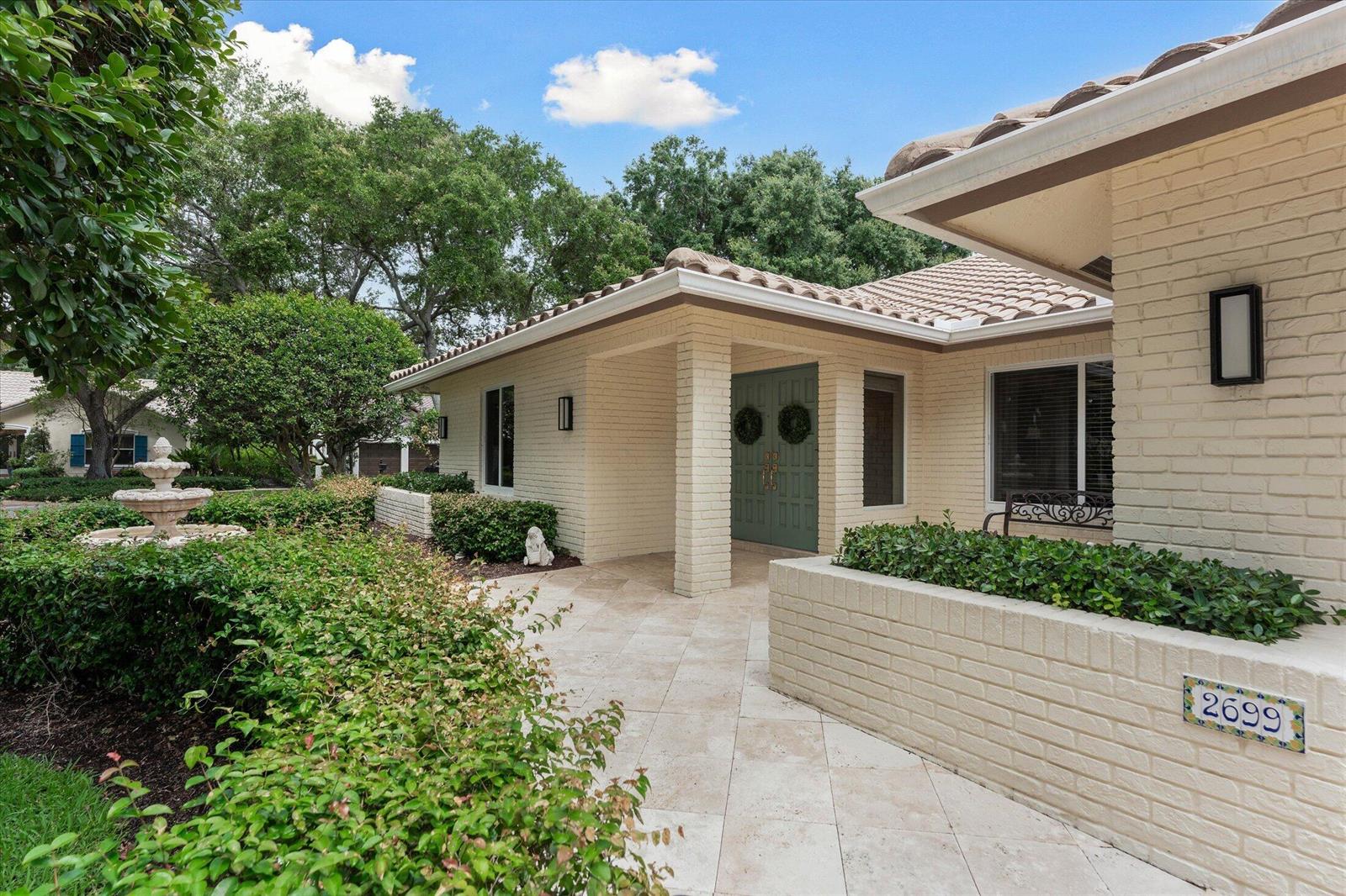 A brick house exterior features a tiled walkway, a stone fountain, and a green door — 2699 NW 38th Street, Boca Raton FL 33434, BOCA RATON, FL