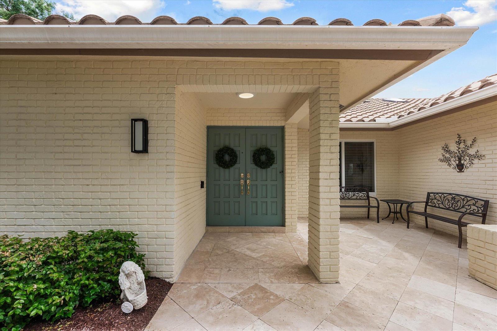 A covered entryway features a teal double door, beige brick walls, and stone tile flooring — 2699 NW 38th Street, Boca Raton FL 33434, BOCA RATON, FL