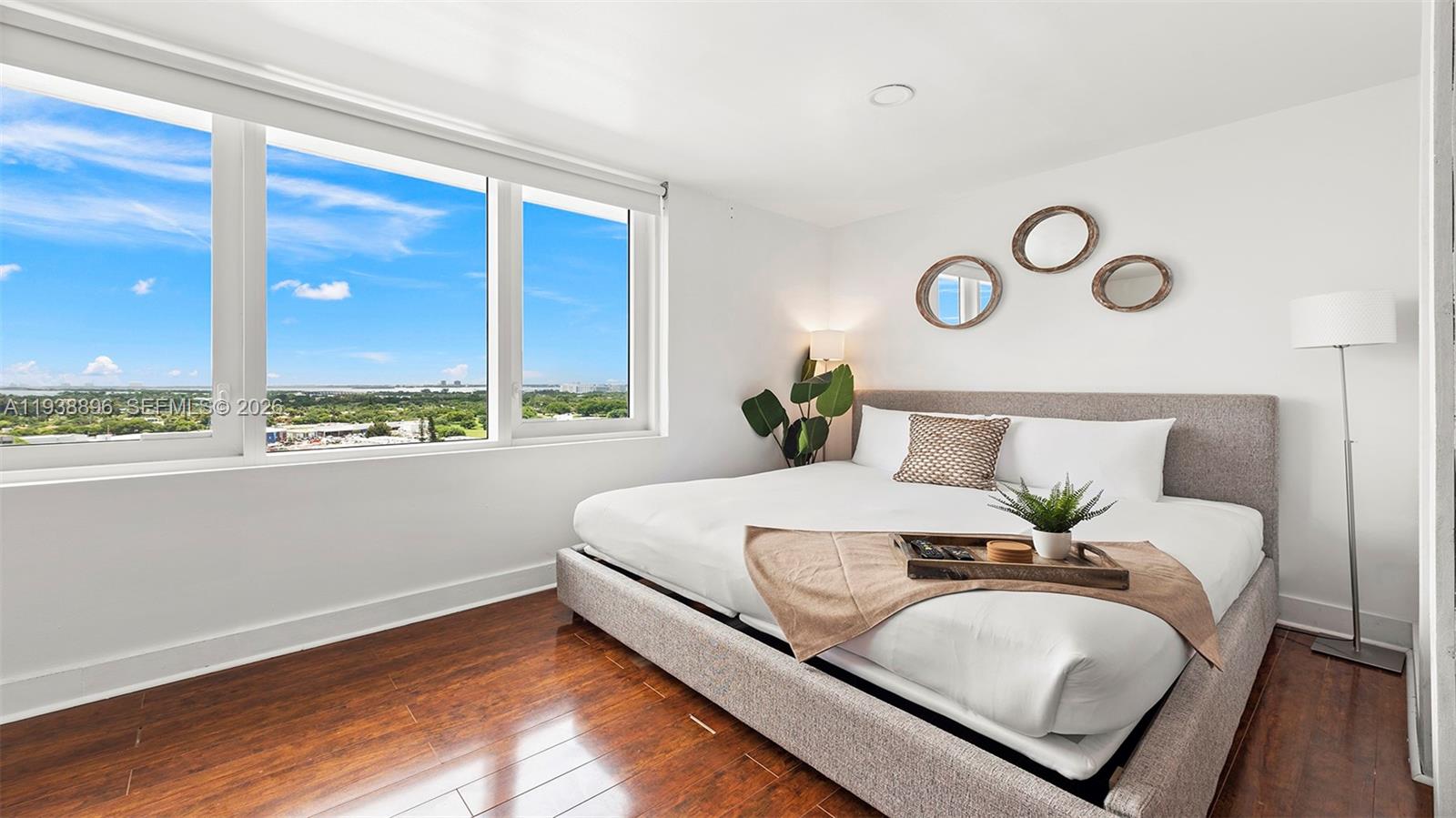 A bedroom features a bed with a gray frame, wood floors, and a large window — 2301 Collins Ave # 1632, Miami Beach FL 33139, MIAMI BEACH, FL