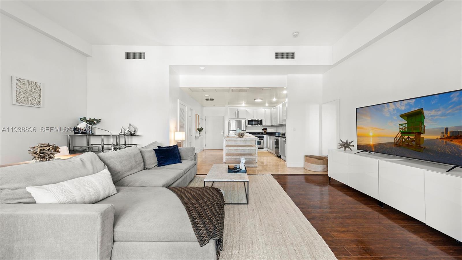 A living room with a grey sectional sofa, a television, and an open-concept kitchen — 2301 Collins Ave # 1632, Miami Beach FL 33139, MIAMI BEACH, FL