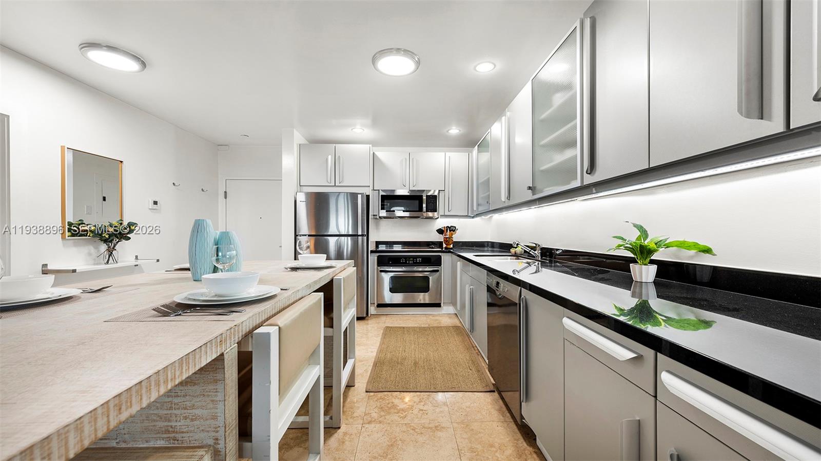 A modern kitchen features light gray cabinetry, black countertops, stainless steel appliances, and a breakfast bar — 2301 Collins Ave # 1632, Miami Beach FL 33139, MIAMI BEACH, FL