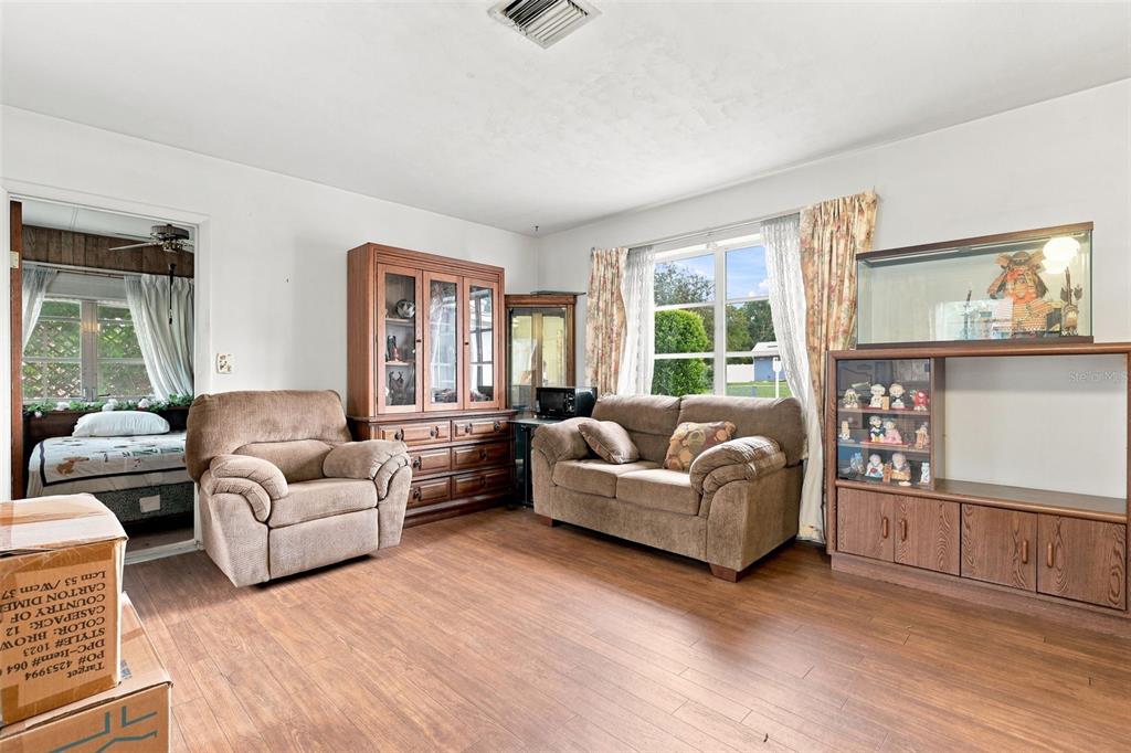 A living room features wood-look flooring, a brown sofa and armchair, and wooden display cabinets — 1119 MAYFLOWER AVENUE, DELTONA, FL