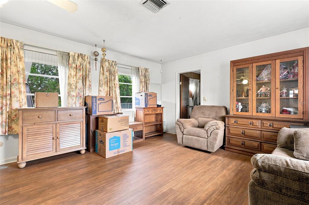 A living room with wood-look flooring, floral curtains, wooden furniture, and several cardboard moving boxes — 1119 MAYFLOWER AVENUE, DELTONA, FL