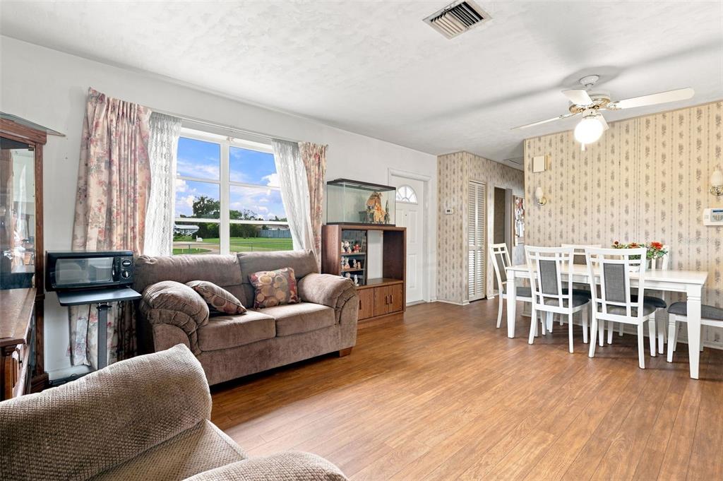 A living and dining room with wood-look flooring, a brown sofa, and floral wallpaper — 1119 MAYFLOWER AVENUE, DELTONA, FL