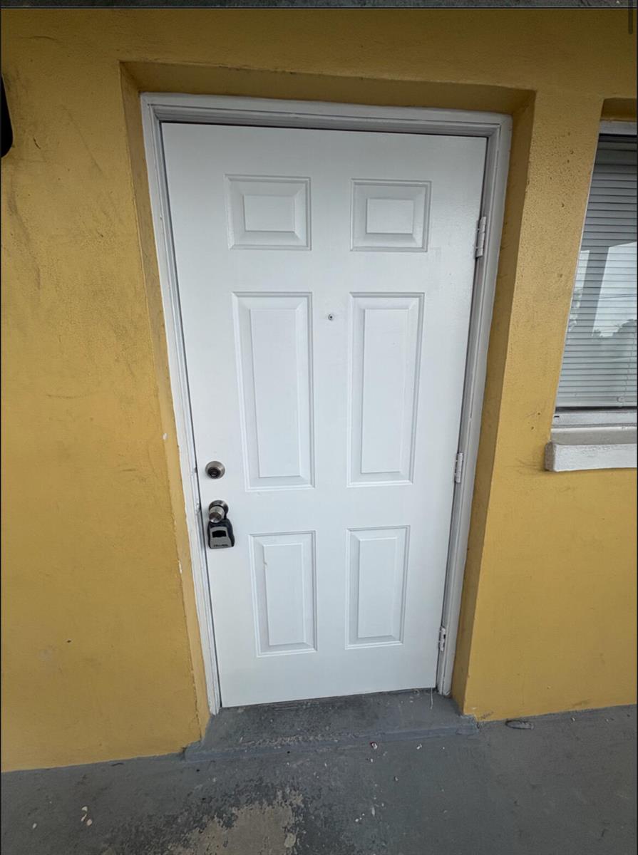 A white six-panel exterior door with a keypad lock is set into a yellow wall — 1501 Crescent Circle # E39, Lake Park FL 33403, LAKE PARK, FL