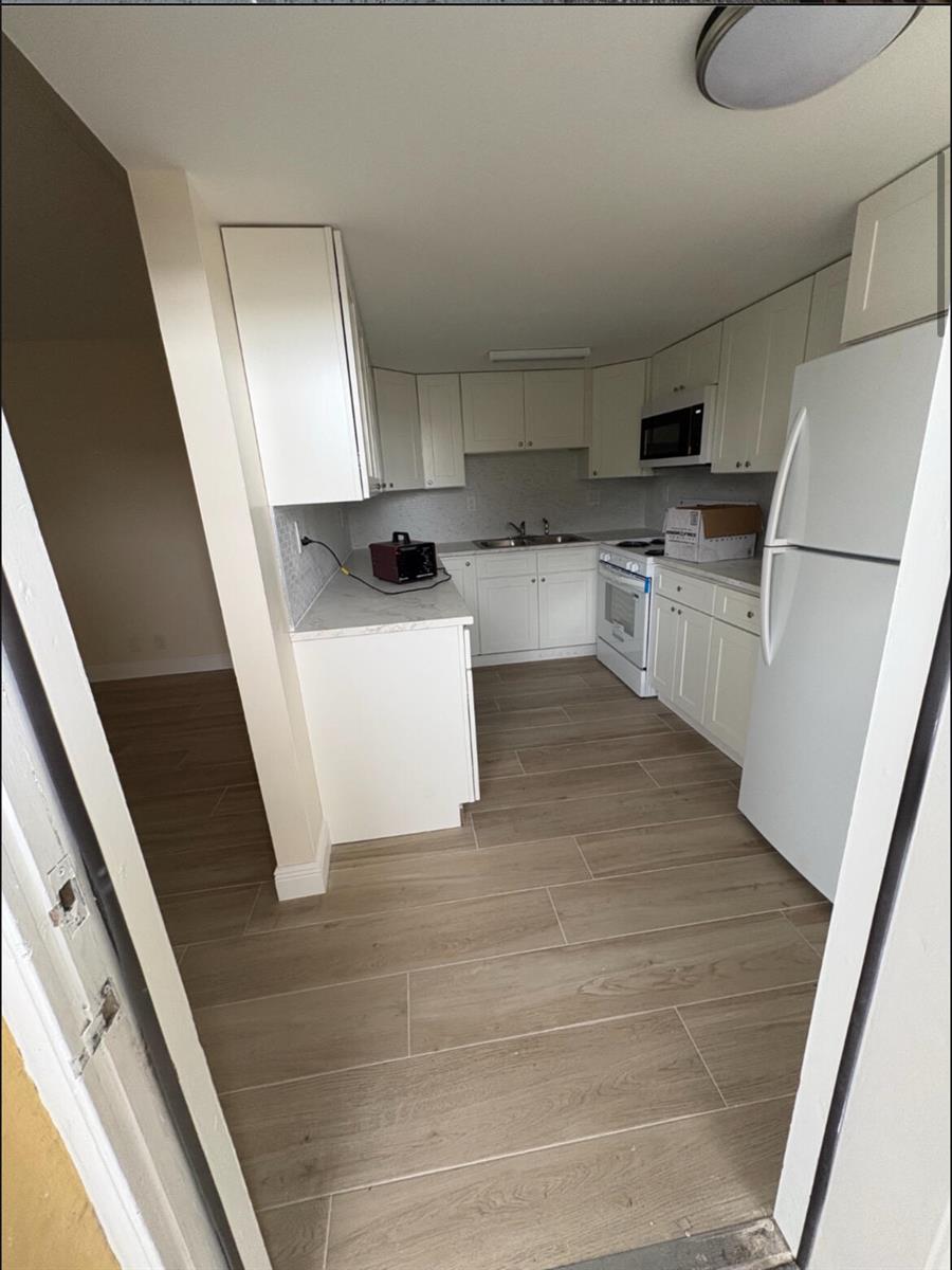 A kitchen with white cabinets, light countertops, and wood-look tile flooring viewed through a doorway — 1501 Crescent Circle # E39, Lake Park FL 33403, LAKE PARK, FL
