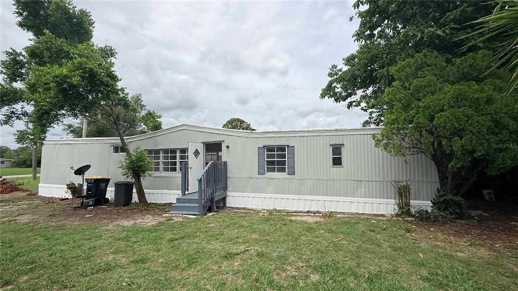 A single-story manufactured home with light-colored siding, a small front porch, and surrounding trees — 115 WHITFIELD STREET, MULBERRY, FL