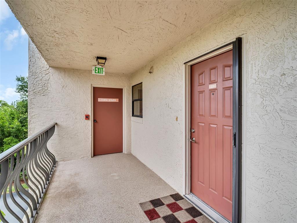 An outdoor apartment hallway features a red door, a stairwell exit, and a metal railing — 504 S FLORIDA AVENUE UNIT 235, TARPON SPRINGS, FL
