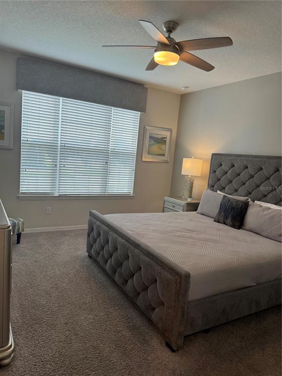 A bedroom features a tufted gray bed, a ceiling fan, and a large window — 9000 EGRET MILLS TERRACE, KISSIMMEE, FL