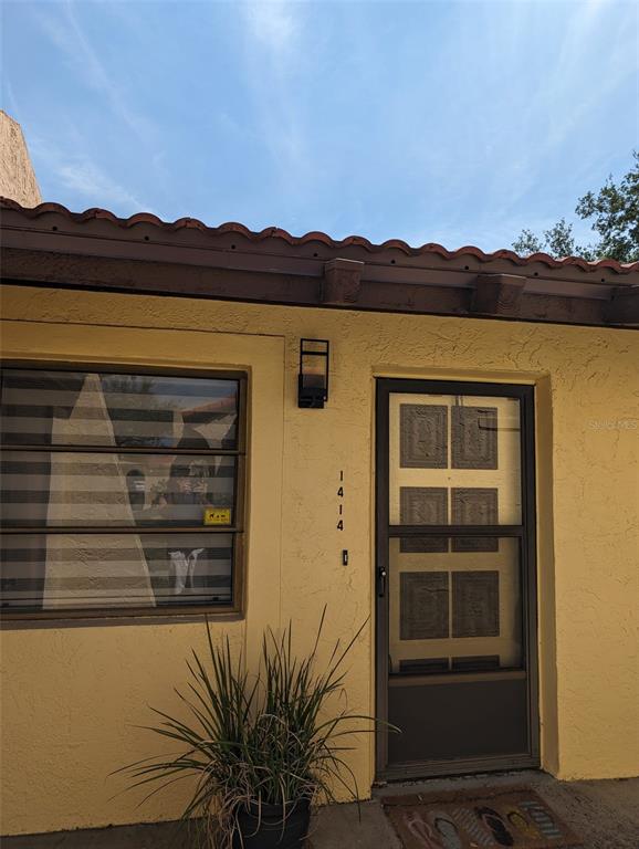 A yellow stucco exterior wall features a window, a door, and a potted plant — 1414 58TH STREET W, BRADENTON, FL