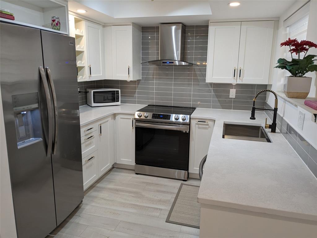 A modern kitchen features white cabinets, stainless steel appliances, gray subway tile, and quartz countertops — 1414 58TH STREET W, BRADENTON, FL