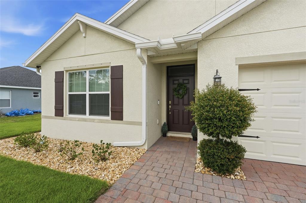 The exterior of a house features a paved walkway leading to a dark brown front door — 1782 YANKEE TERRACE, NORTH PORT, FL