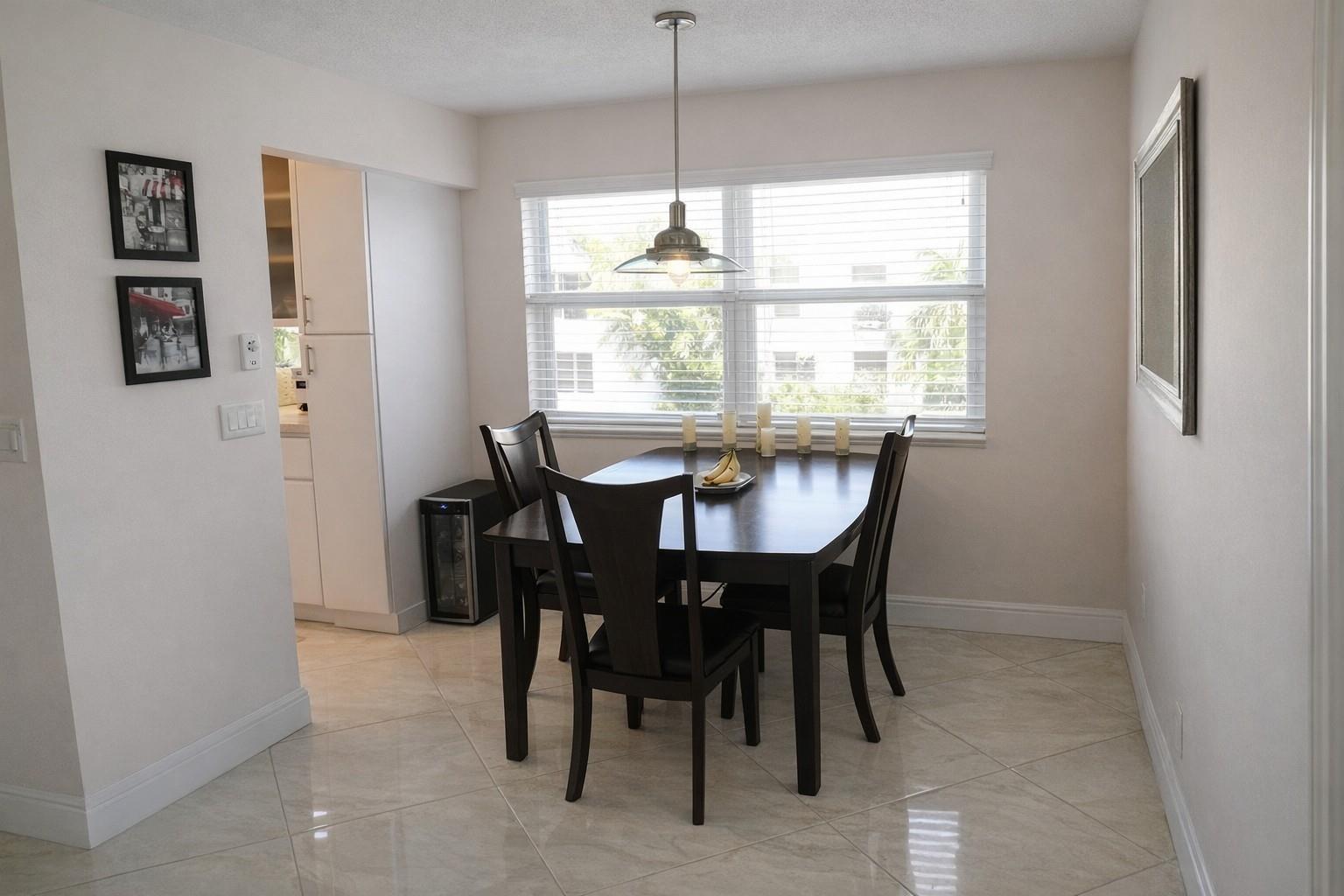 A dining area with a dark wood table, four chairs, and tile flooring near a window — 104 E Windsor E # 104, West Palm Beach FL 33417, WEST PALM BEACH, FL